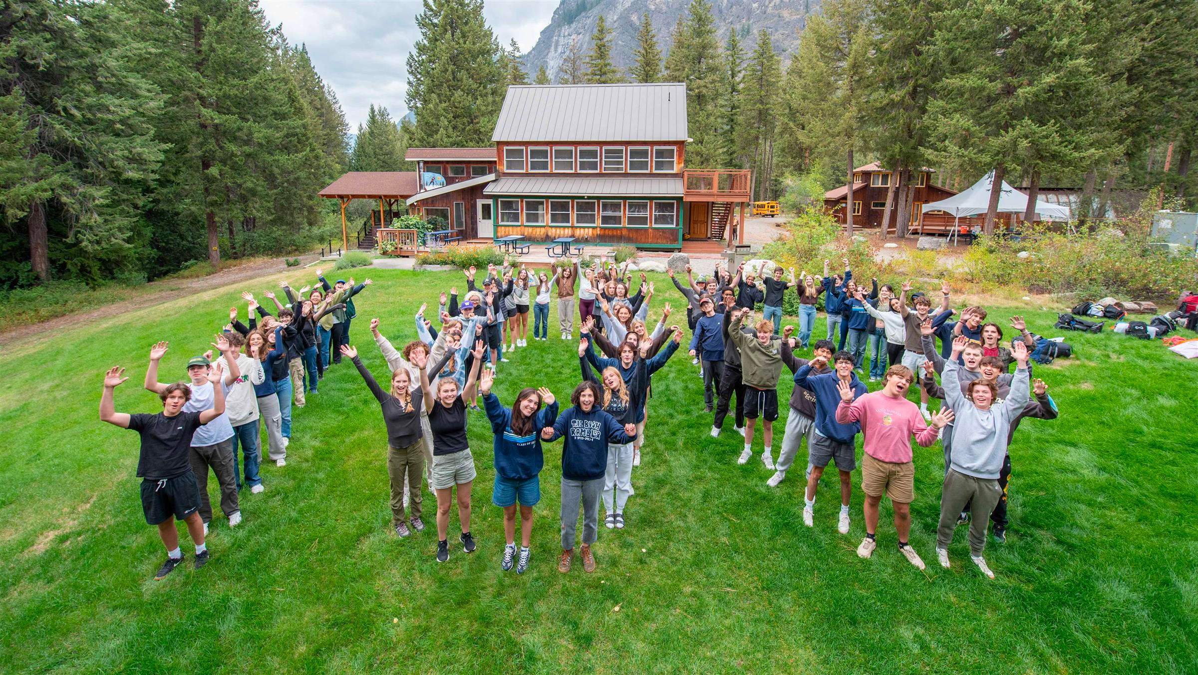 Group of people standing in a formation with their arms up in front of a cabin and trees
